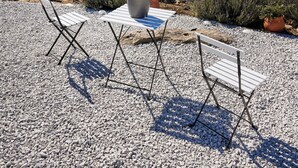 A terrace with two folding chairs, a table, and a potted plant. The terrace overlooks a coastal town with buildings and boats. - Sand Lily Mykonos (Mykonos)