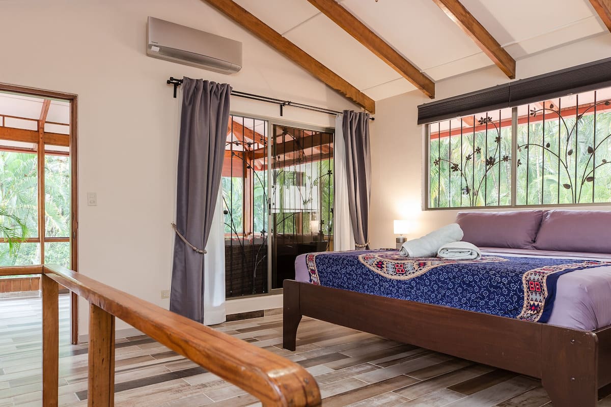 Une chambre à coucher avec un lit, une fenêtre donnant sur un paysage verdoyant, un plafond en bois et une porte coulissante.