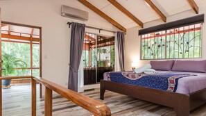 A bedroom with a bed, a window with a view of greenery, a wooden ceiling, and a sliding door.