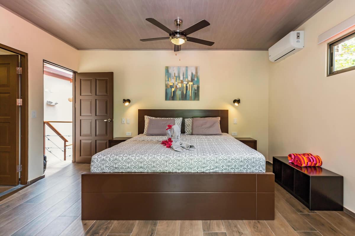 Une chambre à coucher avec un lit, un ventilateur de plafond, un climatiseur, un tableau accroché au mur et une fenêtre.