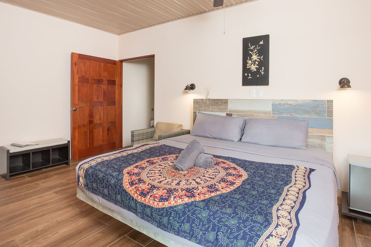 Une chambre à coucher avec un grand lit, une porte en bois, une table de chevet et une œuvre d’art accrochée au mur.