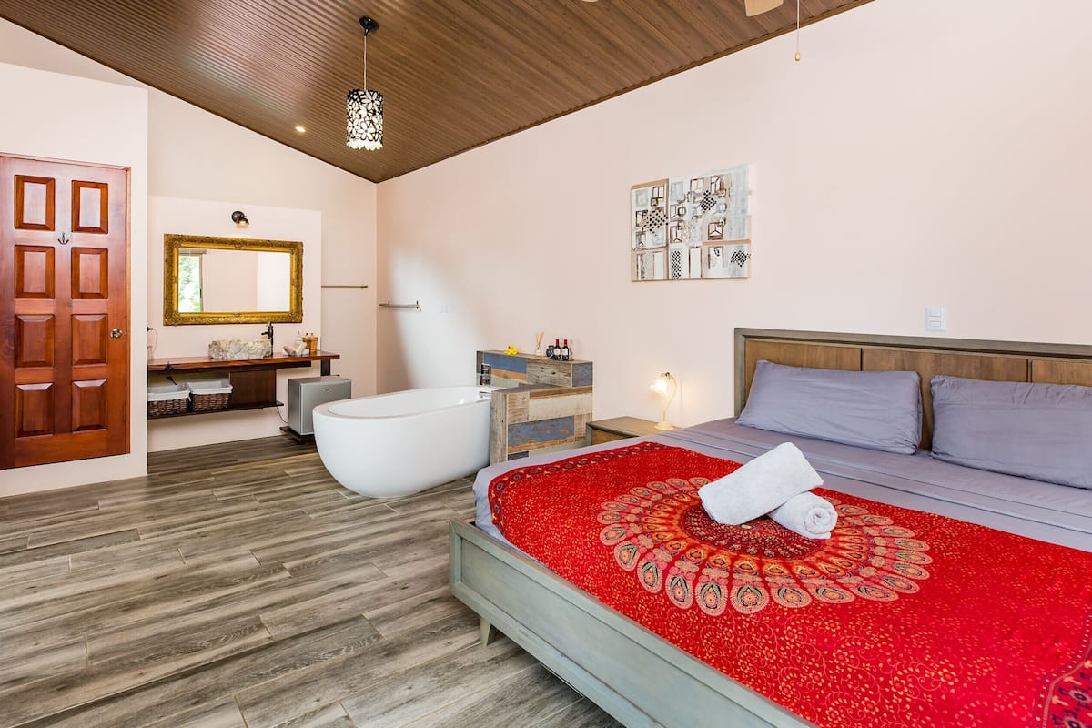 Une chambre avec un grand lit, un plafond en bois, une salle de bain avec une baignoire et un miroir.