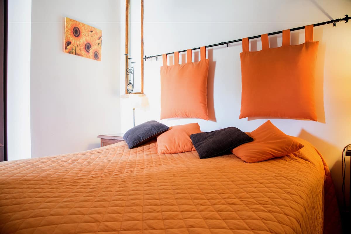 A bed with an orange quilted bedspread, two black pillows, and three orange pillows.