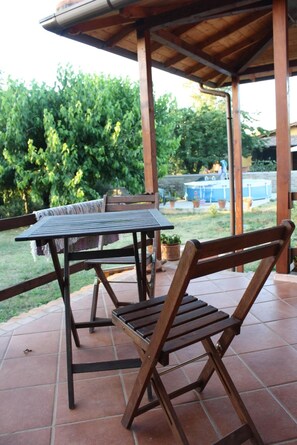 Un patio al aire libre con mesa y sillas de madera, rodeado por una pérgola de madera y un piso de baldosas.