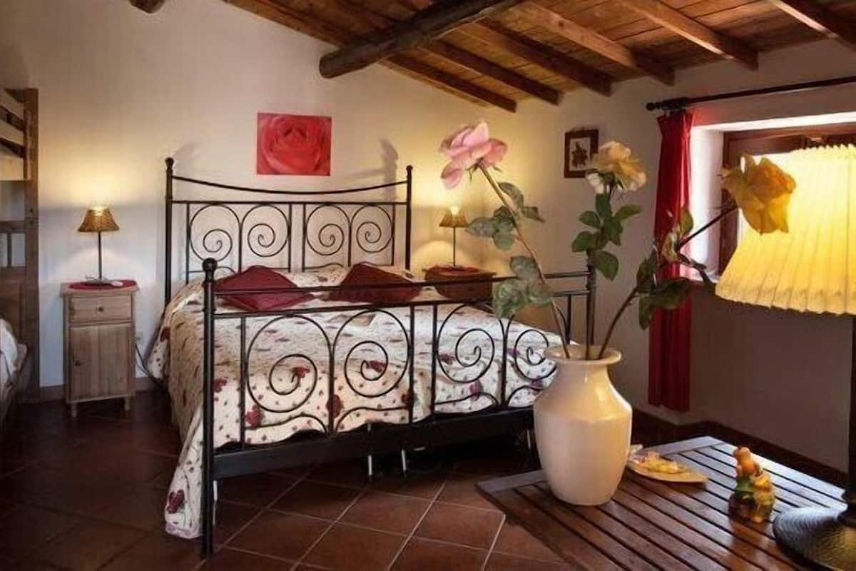 A bedroom with a bed, a nightstand, a vase with flowers, and a window with curtains.