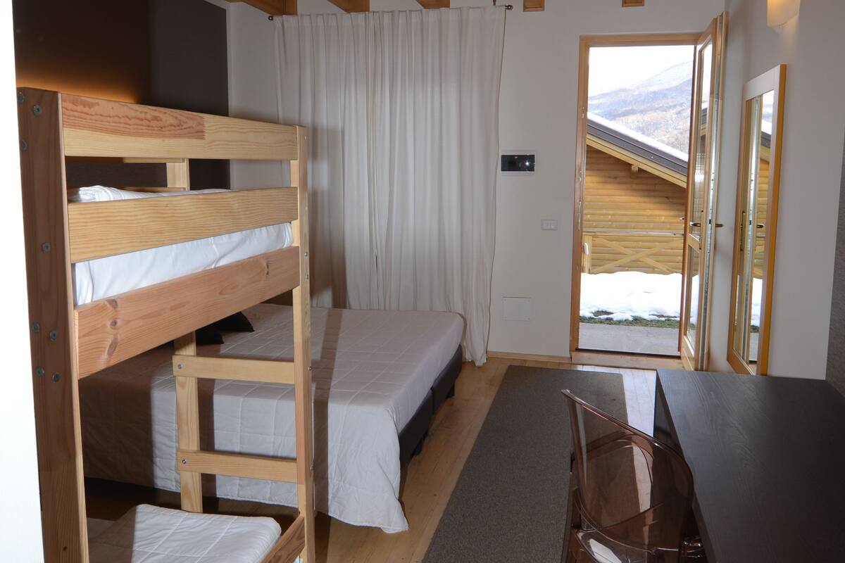 A room with wooden bunk beds, a desk, and a chair.