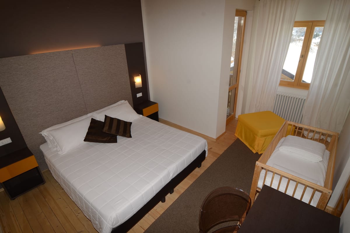A hotel room with a large bed, a small table, a chair, a nightstand, and a window with curtains.