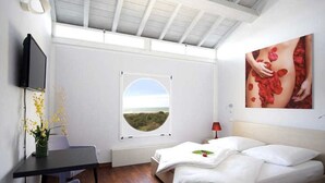 Een slaapkamer met een bed, bureau, stoel, televisie, een raam met uitzicht en een schilderij aan de muur.