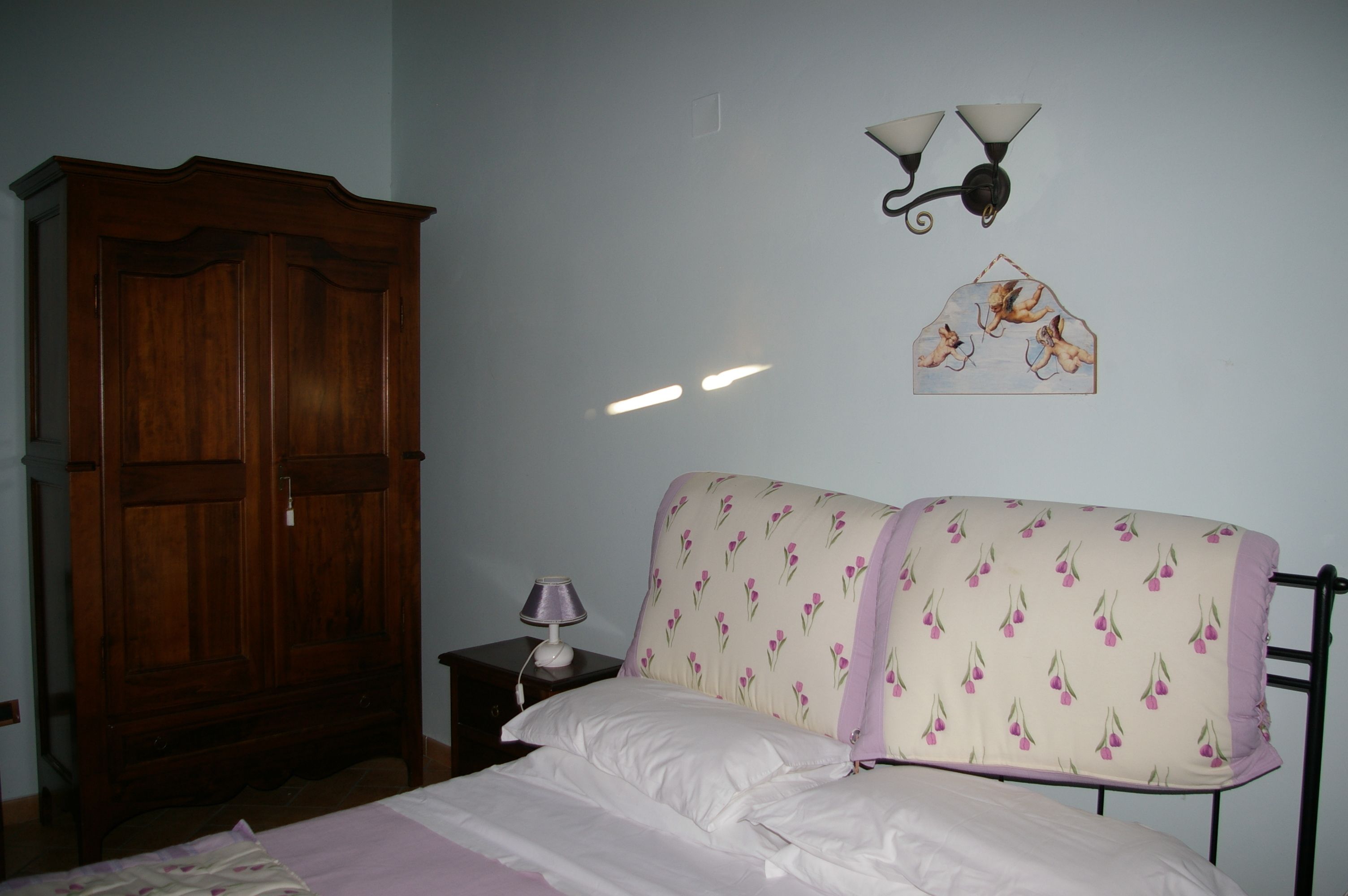 Quarto com cama, mesa de cabeceira, guarda-roupa de madeira e iluminação embutida na parede.