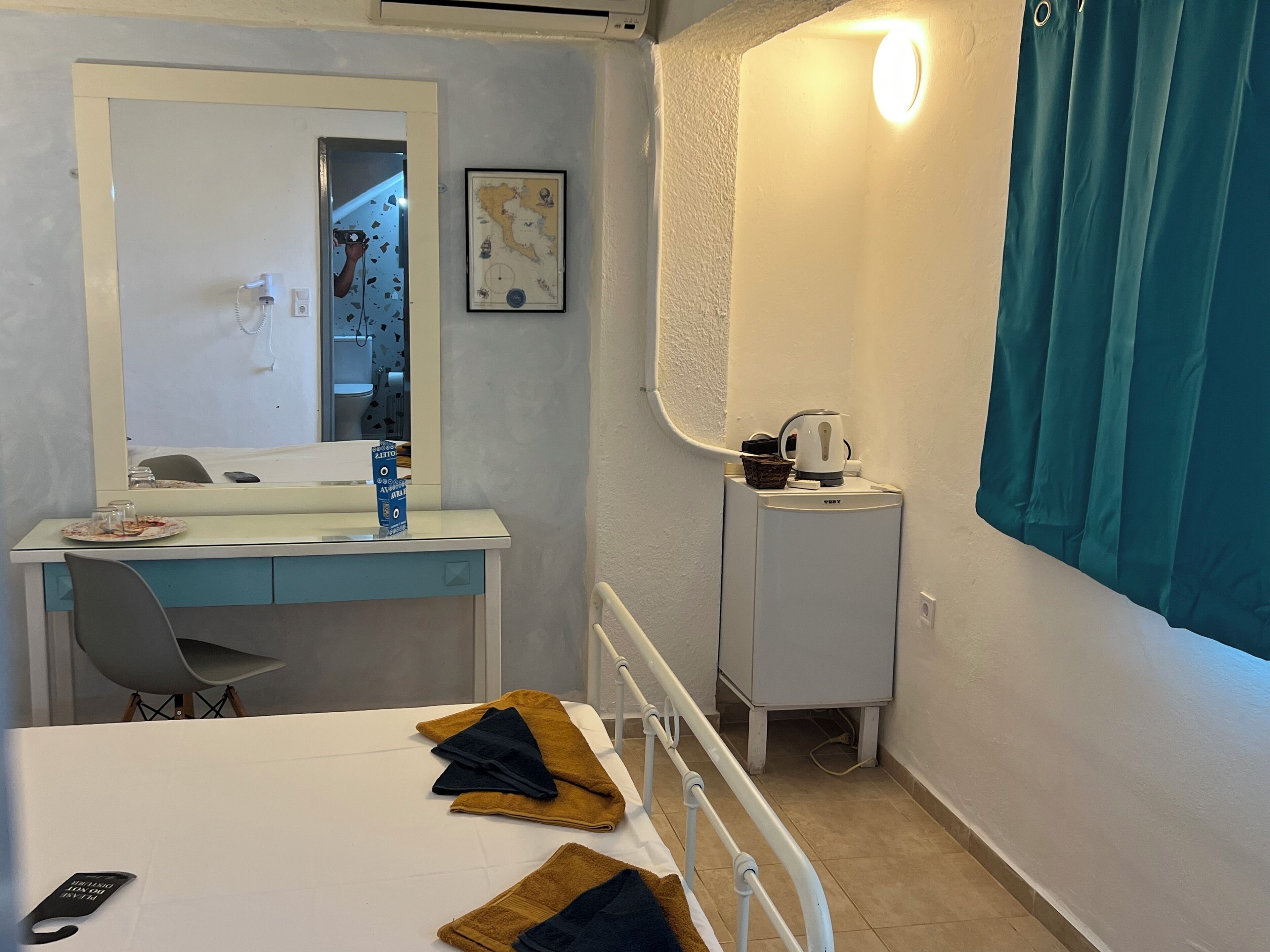 A hotel room with a bed, a desk with a mirror, a small cabinet, and a window with curtains.