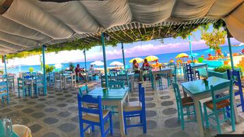 An outdoor dining area with tables and chairs, a view of the sea, and umbrellas.