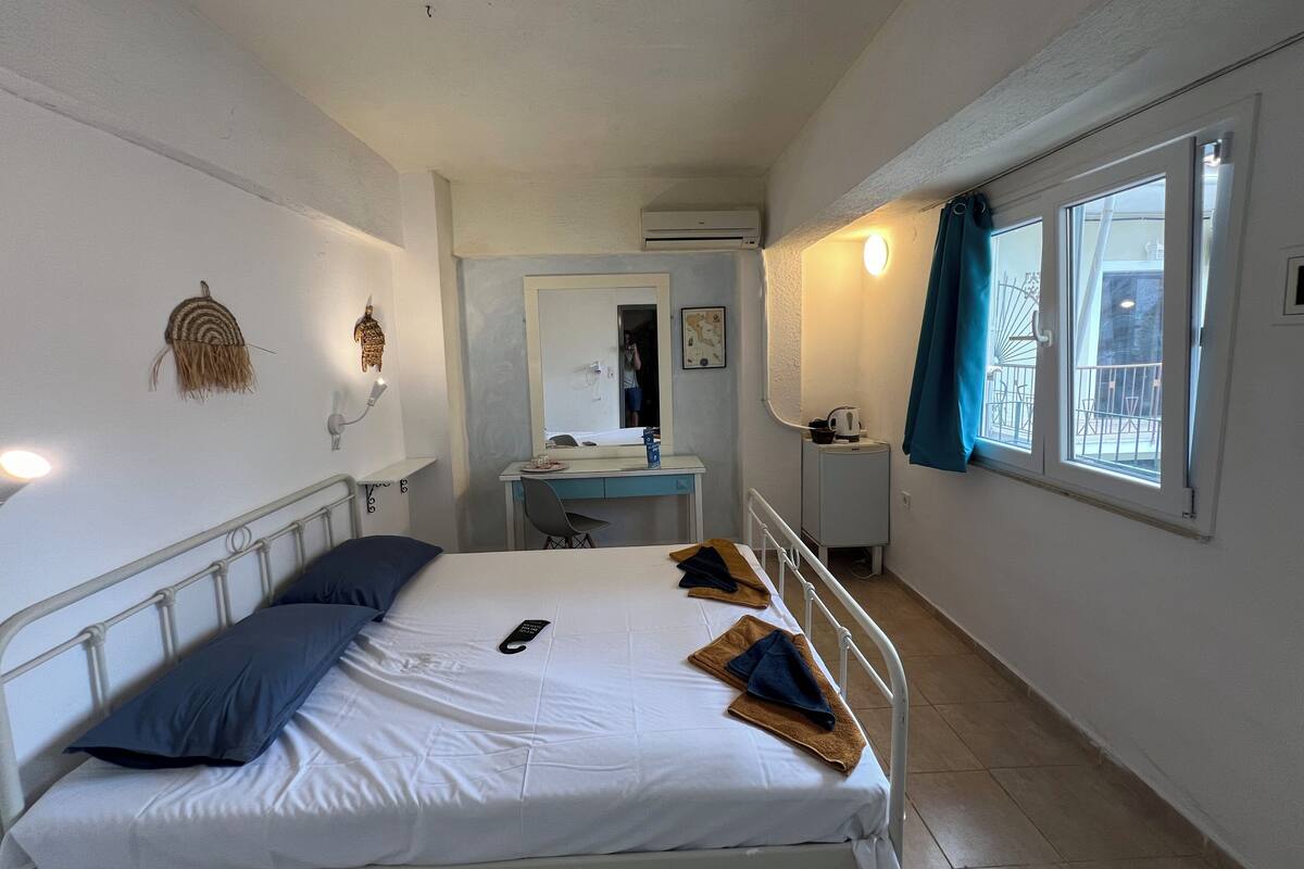 A bedroom with a bed, a desk, a mirror, and a window with curtains.