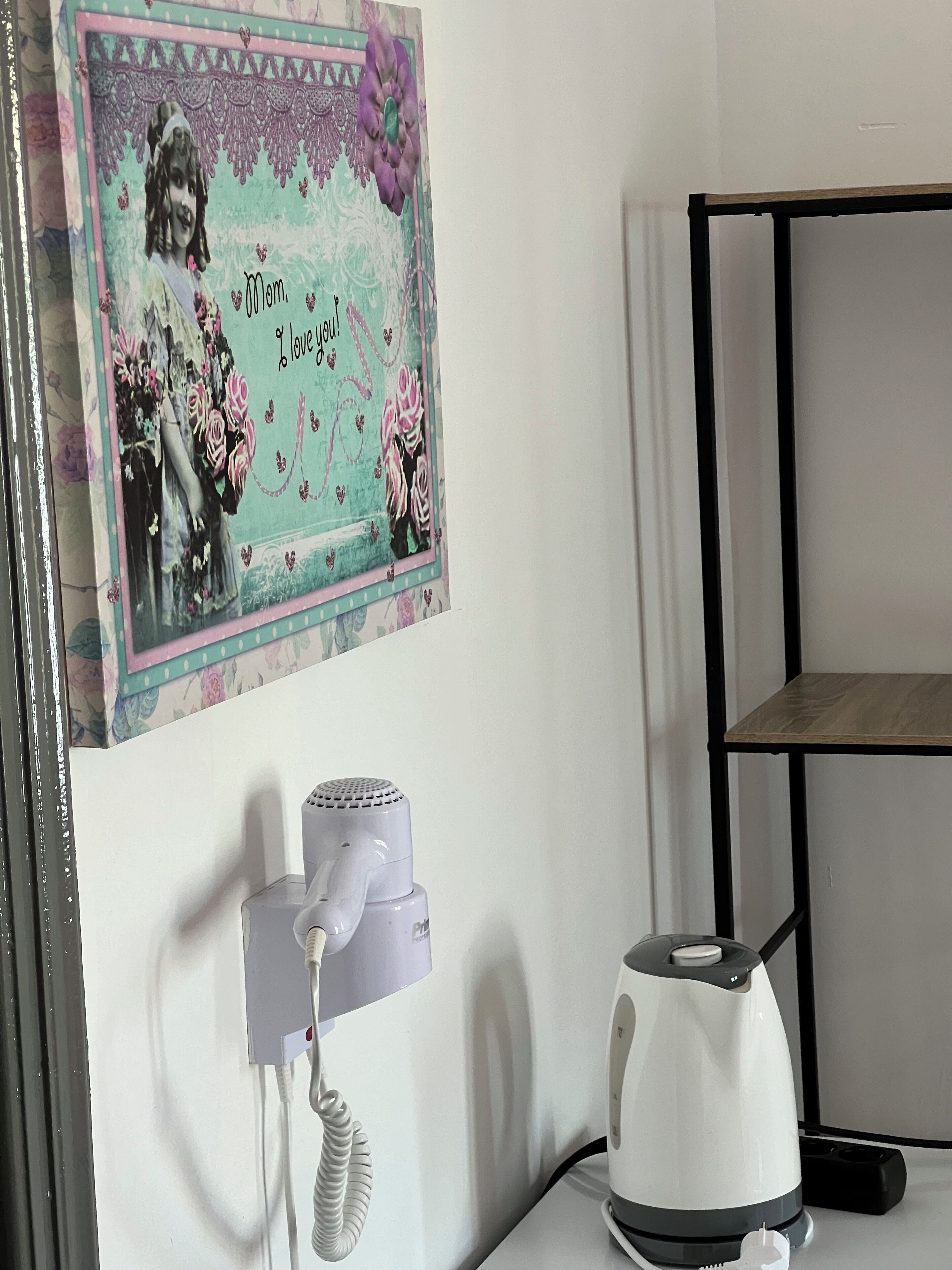 A wall with a decorative card featuring a woman and roses, a white phone, and a kettle on a table.