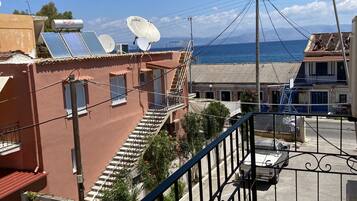 A residential area with a balcony overlooking a street, solar panels on a building, and a clear view of the sea.