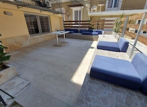 An outdoor patio with stone flooring, blue cushioned seating, and a table. - Avra Boutique (Corfu)