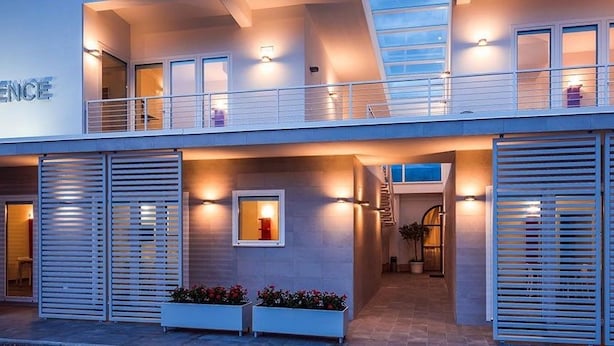 Un edificio moderno con un letrero que dice "RESIDENCE". Cuenta con un balcón con barandillas, una escalera y una entrada bien iluminada.