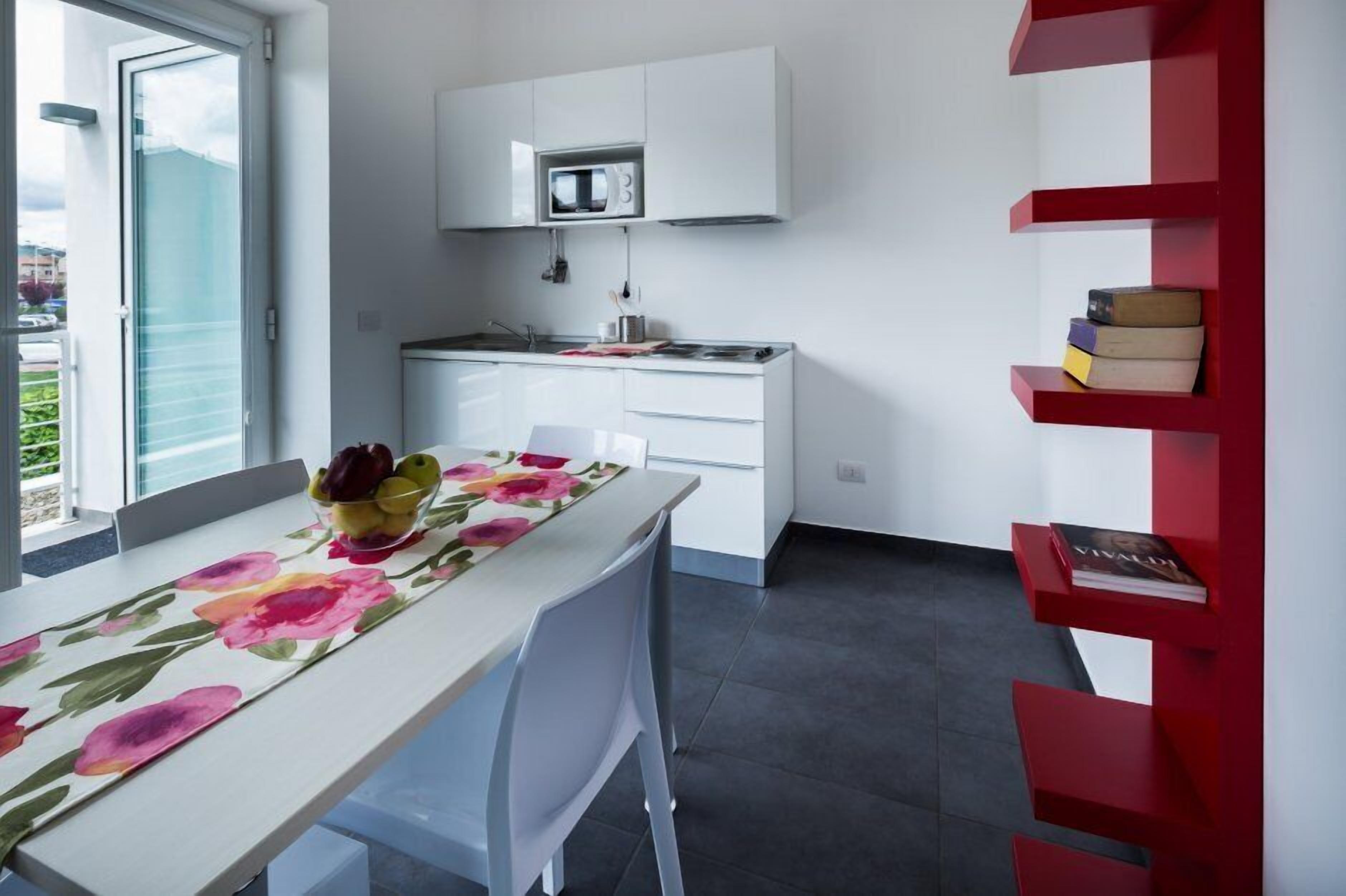 Une cuisine moderne avec des meubles blancs, un four à micro-ondes et une bibliothèque rouge.