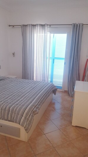 A bedroom with a bed, curtains, a window, and a dresser.