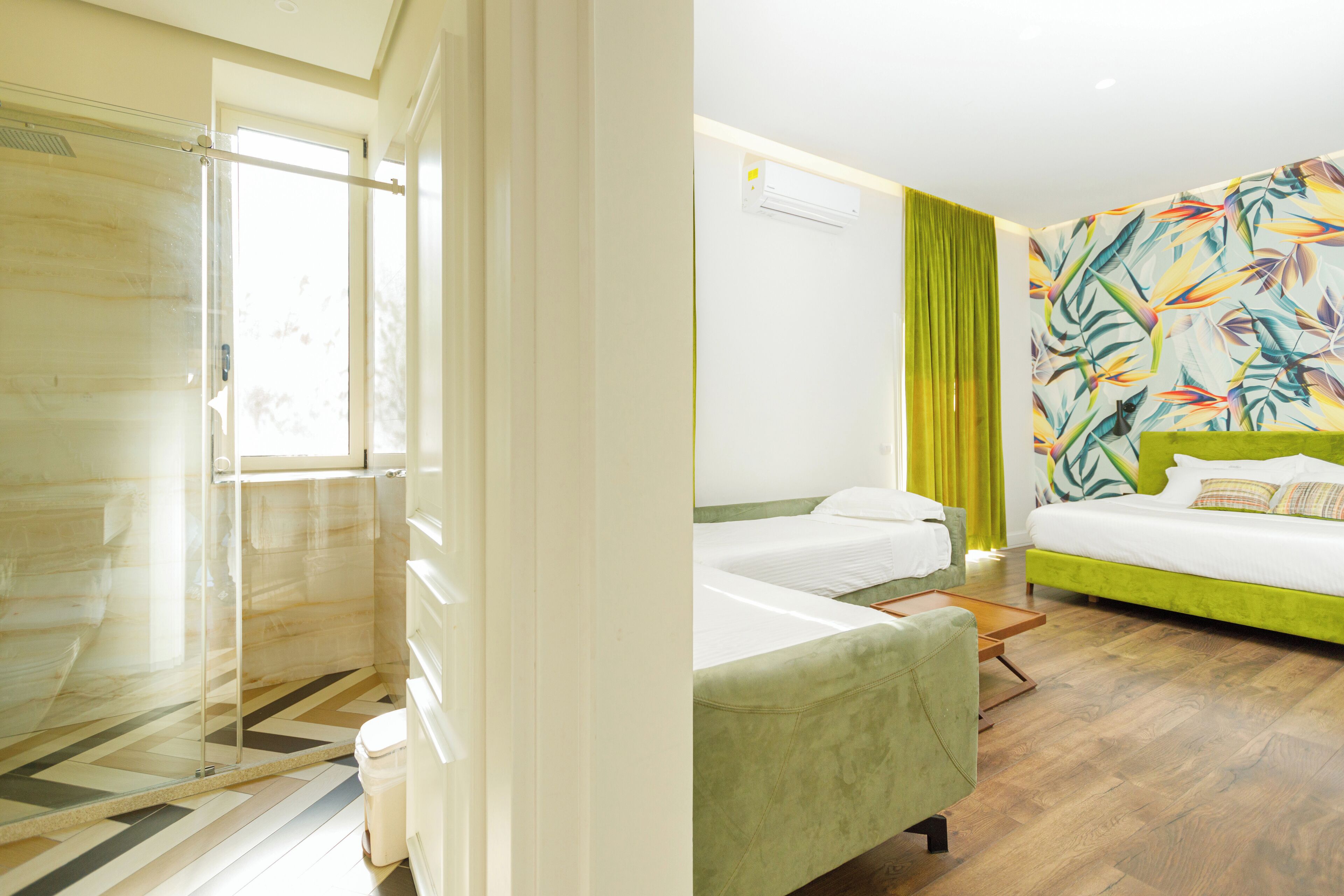 Una habitación de hotel con ducha, cama con cabecera verde y un mural de pared colorido.