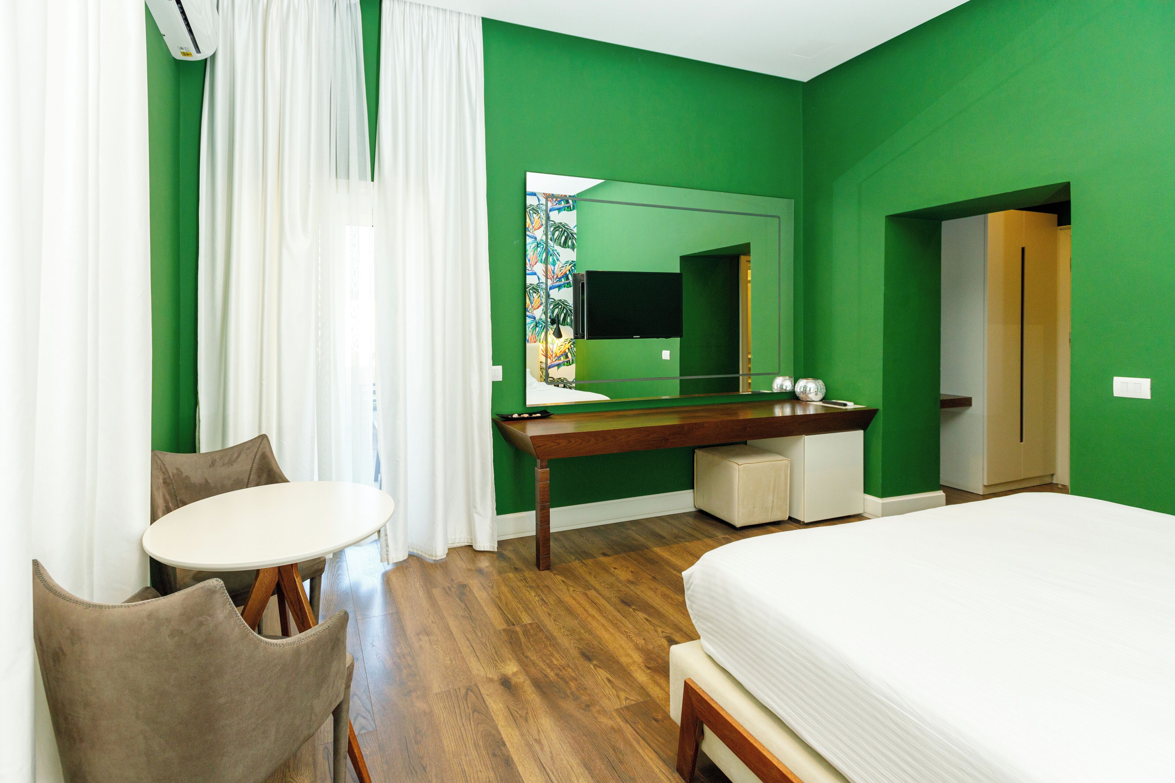 A hotel room with a bed, a desk, a chair, a mirror, and a television.