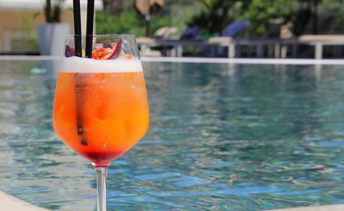 En cocktail i et glas med sugerør, placeret ved en pool.