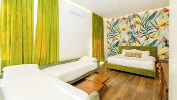 A hotel room with two single beds, a green sofa, a wooden side table, and a colorful tropical wallpaper.