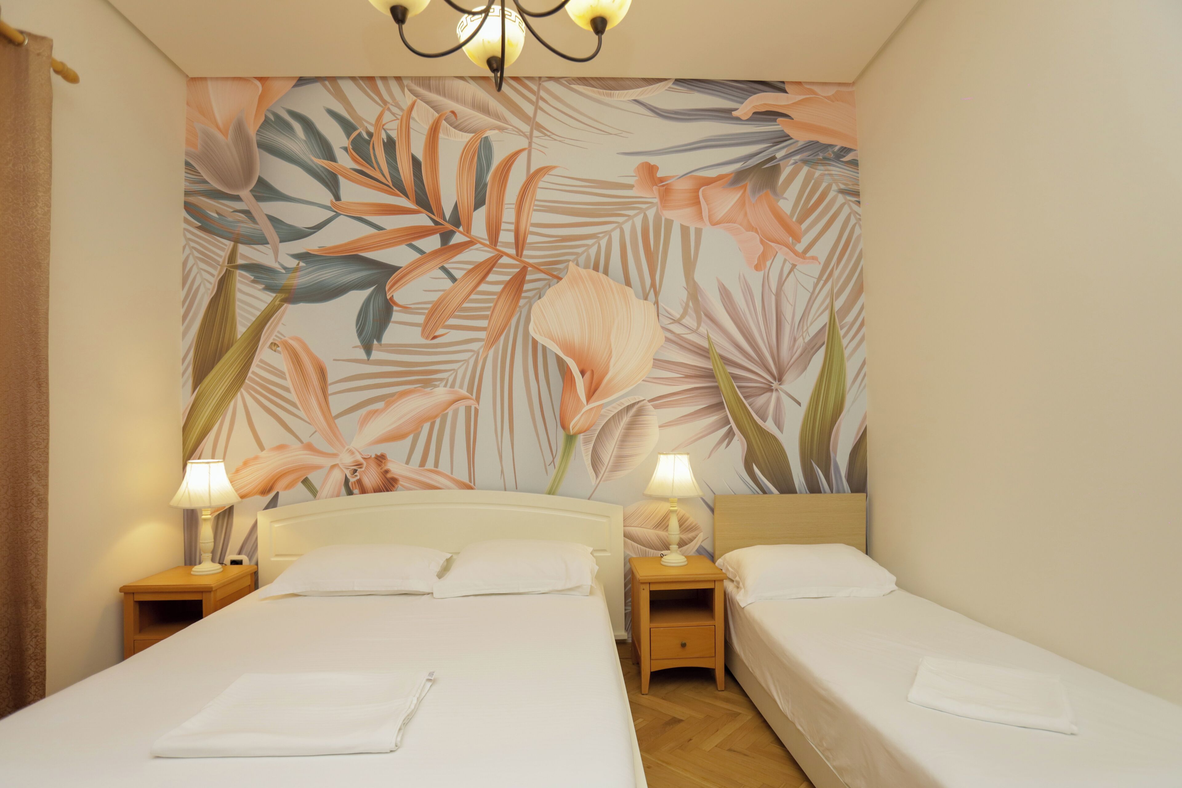 Ein Hotelzimmer mit zwei Betten, einer Wandmalerei mit Blumenmotiv und zwei Nachttischlampen.