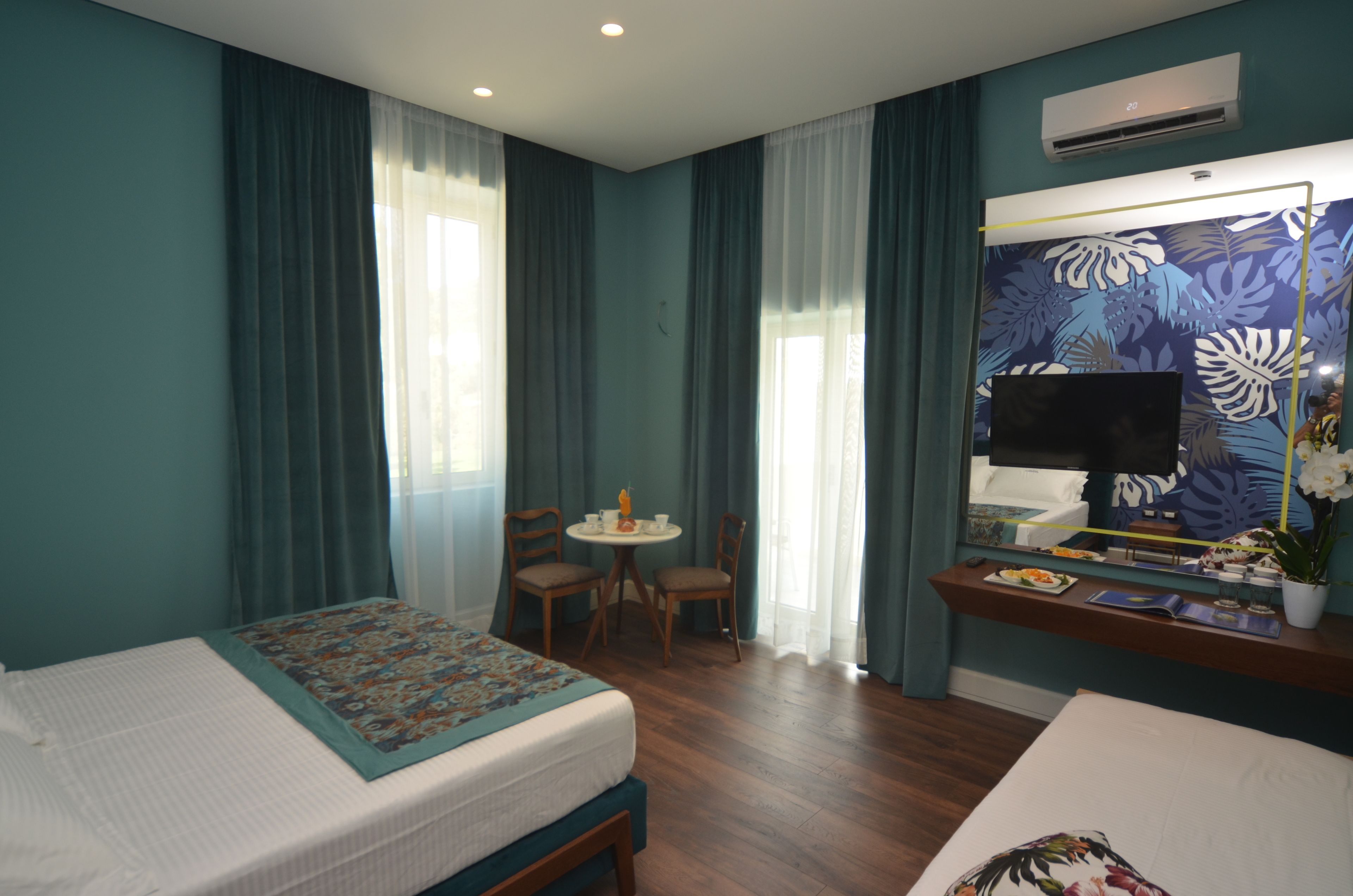 A hotel room with two beds, a small table with chairs, a TV, and a mirror.