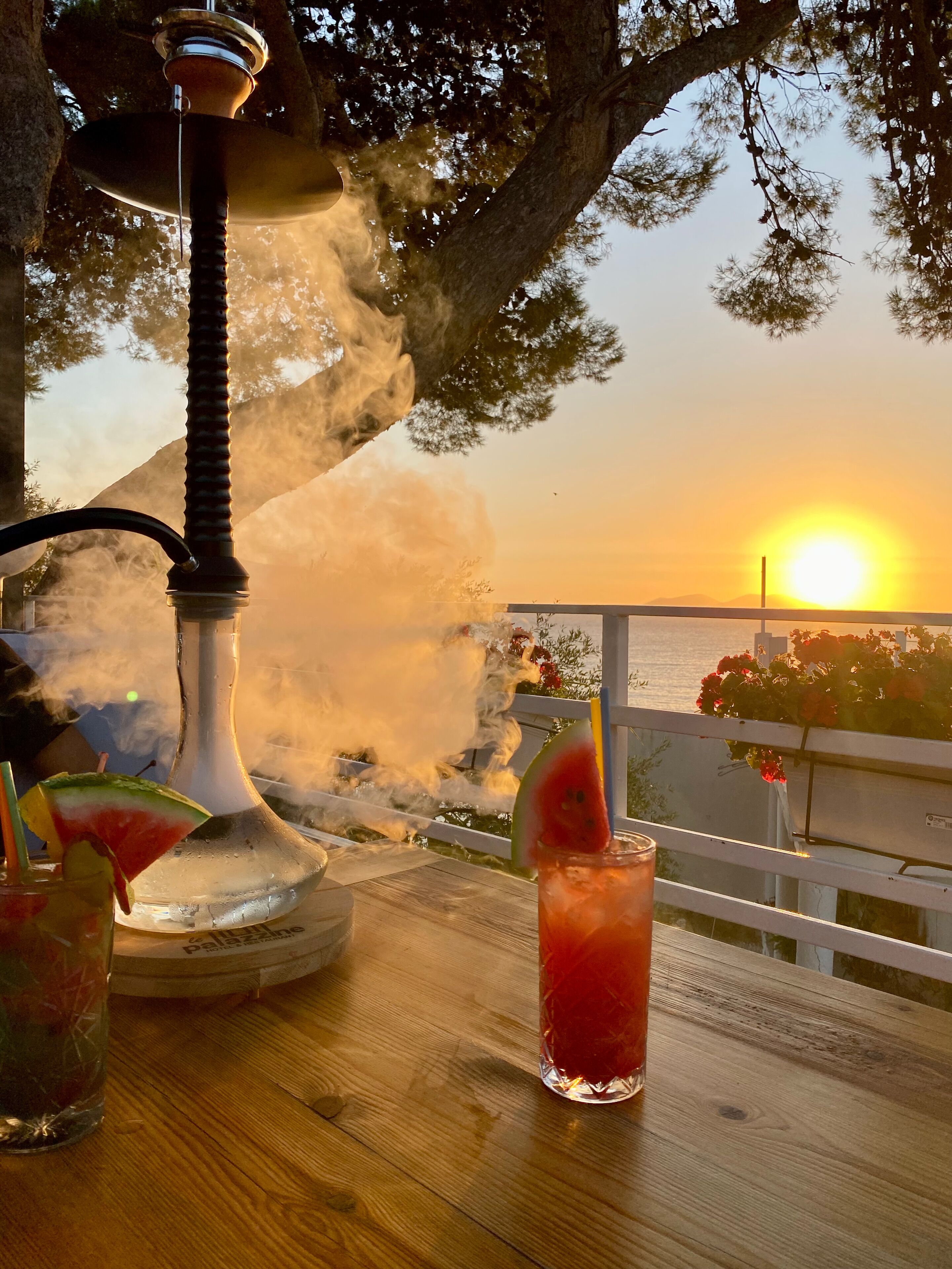 A wooden table with a hookah, a glass of red drink, and a slice of watermelon.