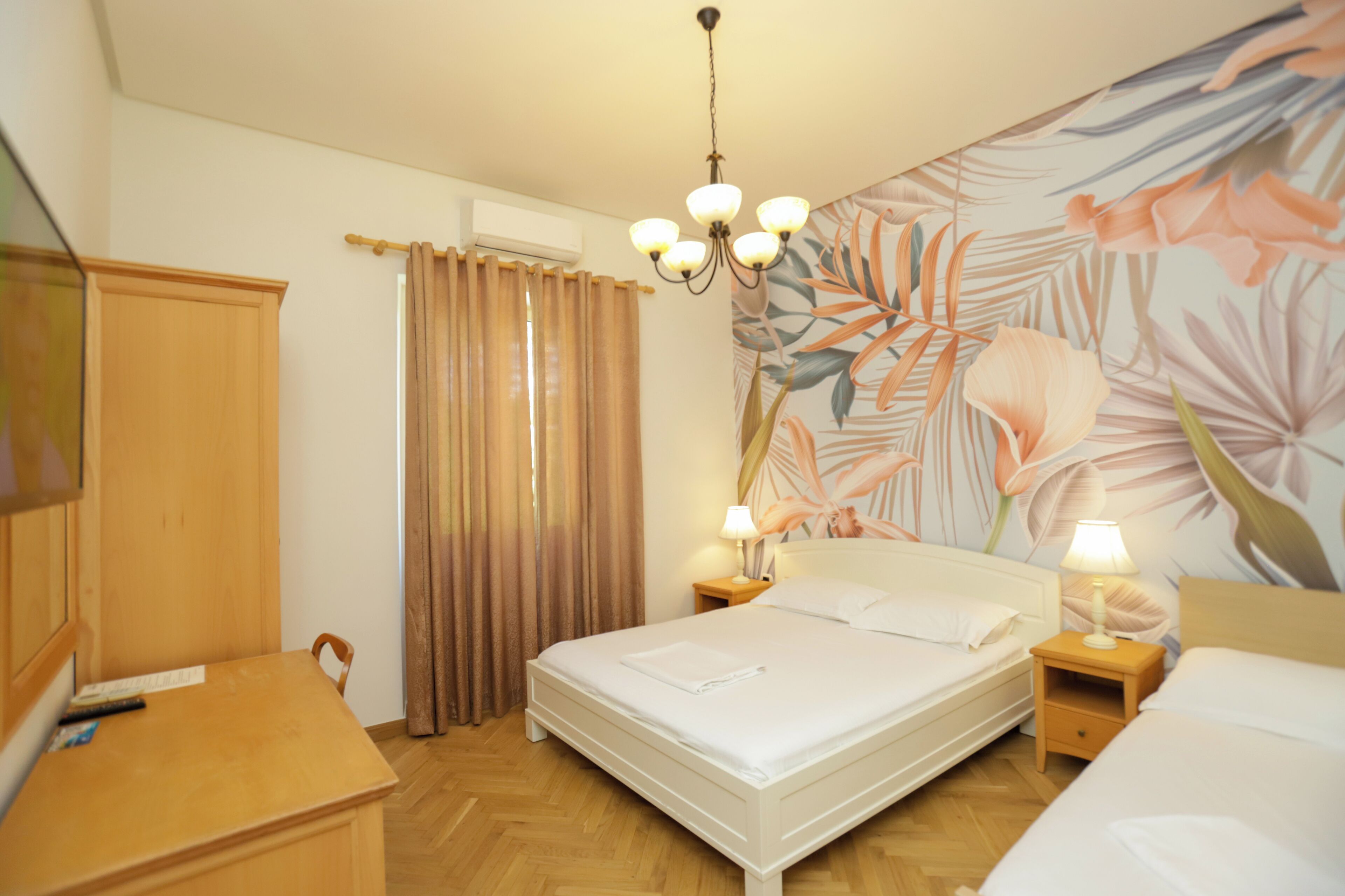 A hotel room with a large bed, two bedside tables with lamps, a wooden wardrobe, a curtain, and a floral wall mural.