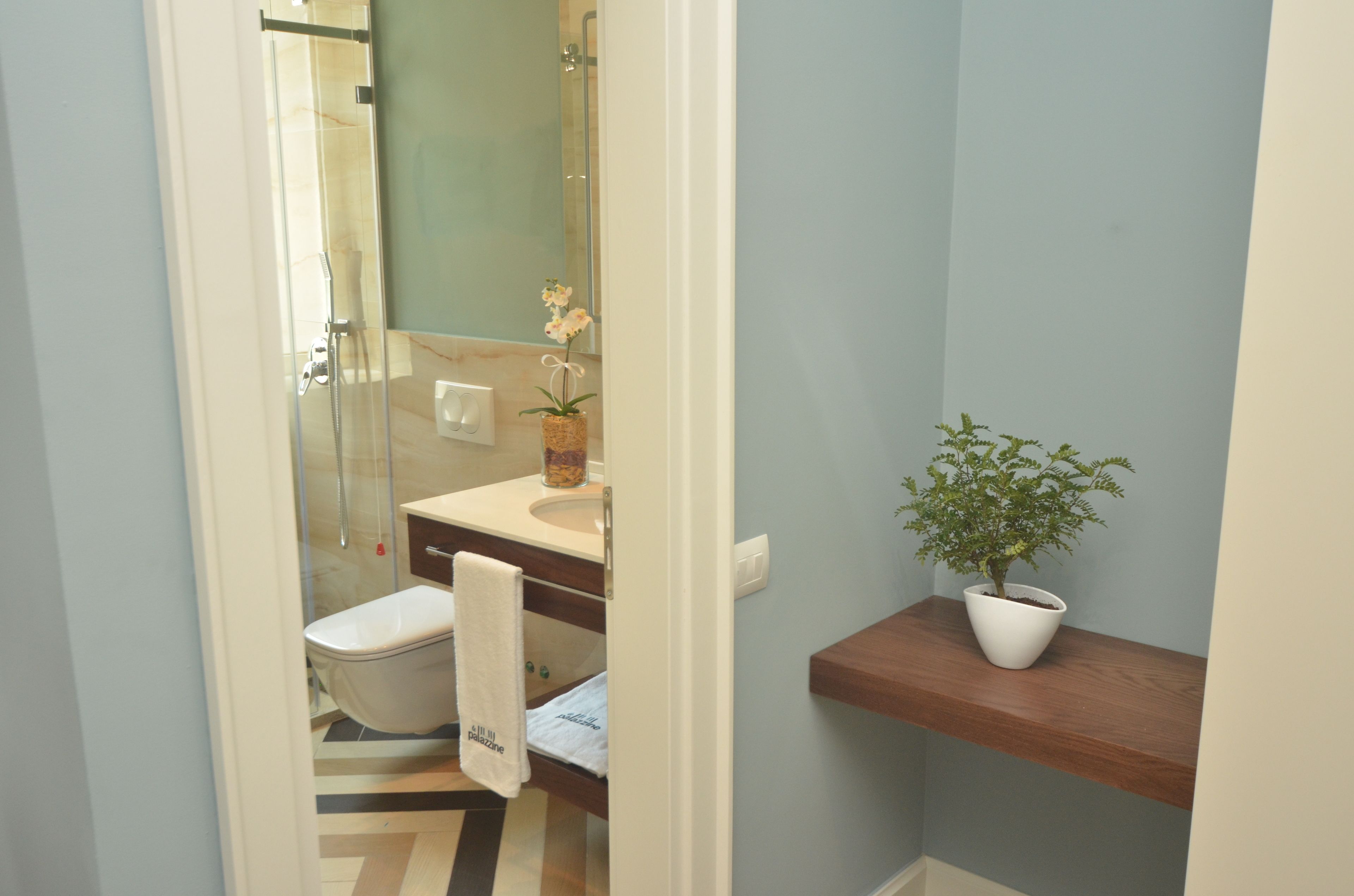 Un baño con cabina de ducha de vidrio, un lavabo con un jarrón de flores, un inodoro y una planta en maceta sobre una estantería.