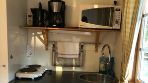 A compact kitchen with a microwave, kettle, and coffee maker on a shelf, a sink, and a compact refrigerator. - Korskullens Camping Stugor & Cafe (Soderkoping)