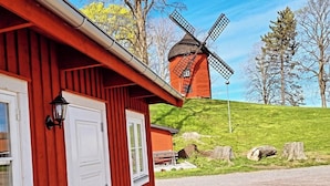 A red wooden building with a white door and windows, a windmill in the background, and a grassy hill. - Korskullens Camping Stugor & Cafe (Soderkoping)