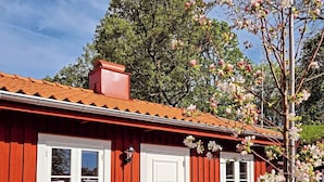 A red wooden house with a tiled roof, a white door, and windows. There is a bench and a table outside. - Korskullens Camping Stugor & Cafe (Soderkoping)