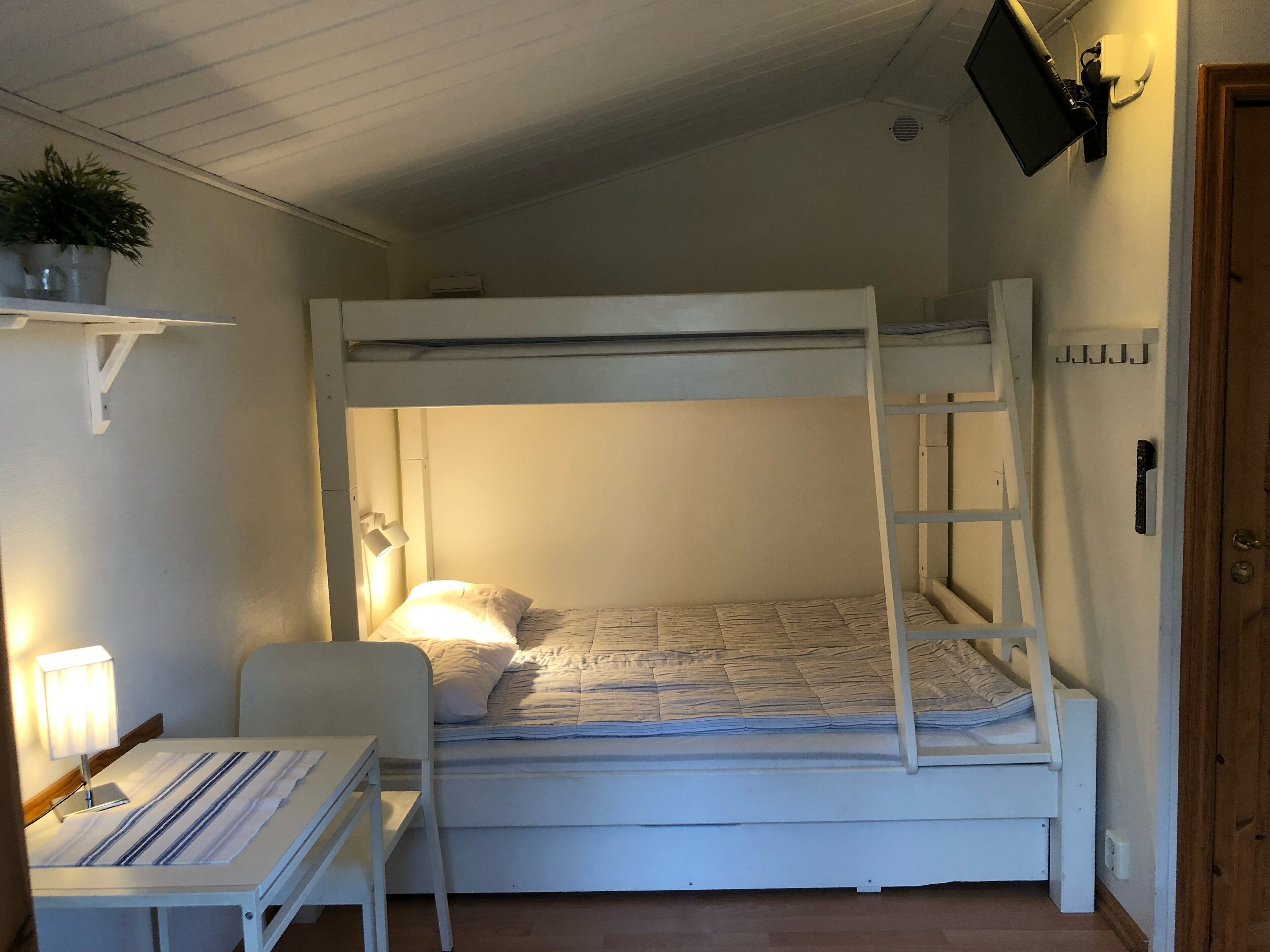 A bunk bed room with a desk and chair, a bedside lamp, and a TV mounted on the wall.