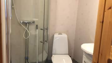 Een compacte badkamer met een douchecabine van glas, een wit toilet en een klein kastje.