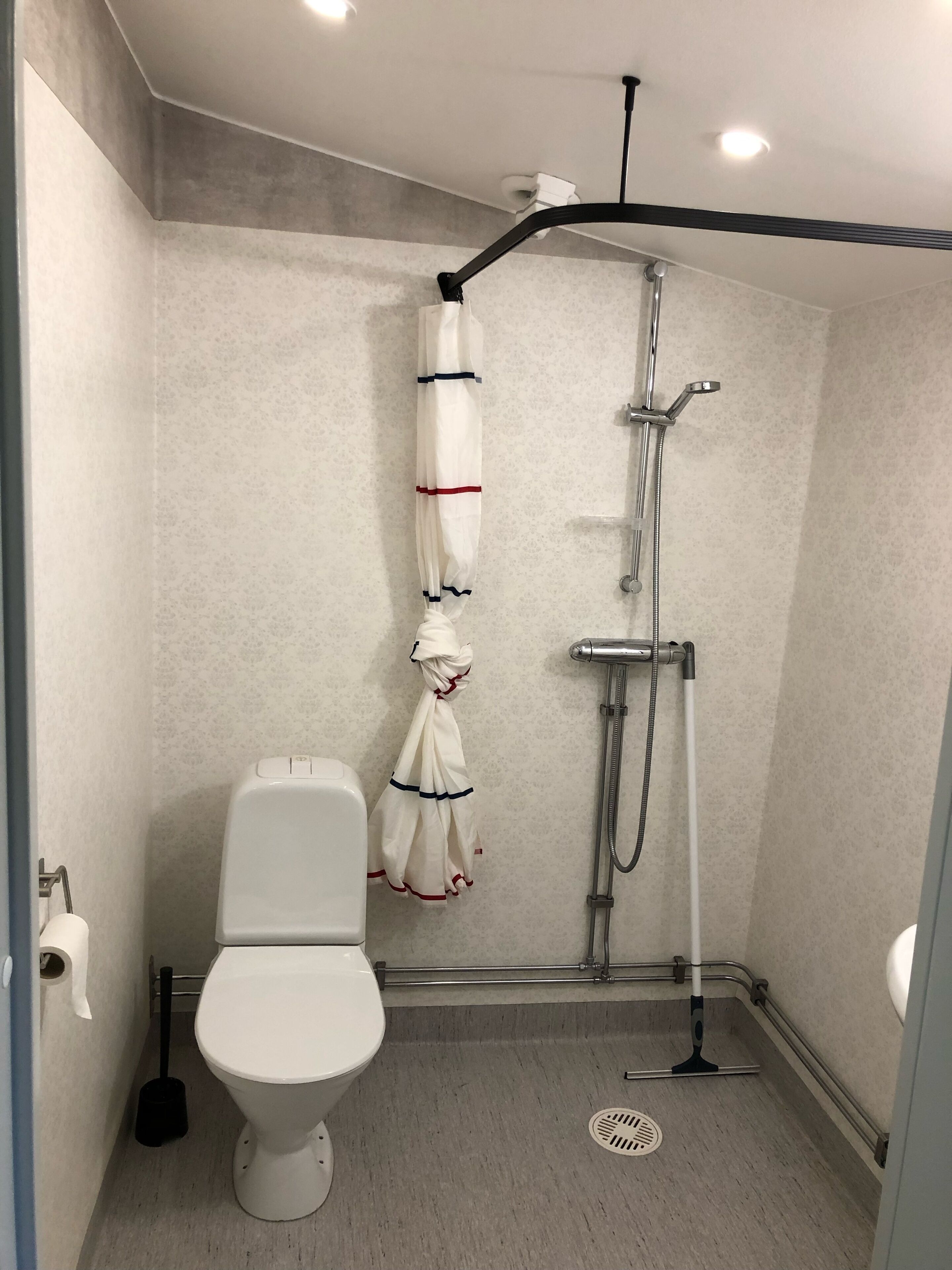Une petite salle de bain moderne, équipée de toilettes, d’une douche et d’une serviette accrochée au mur.