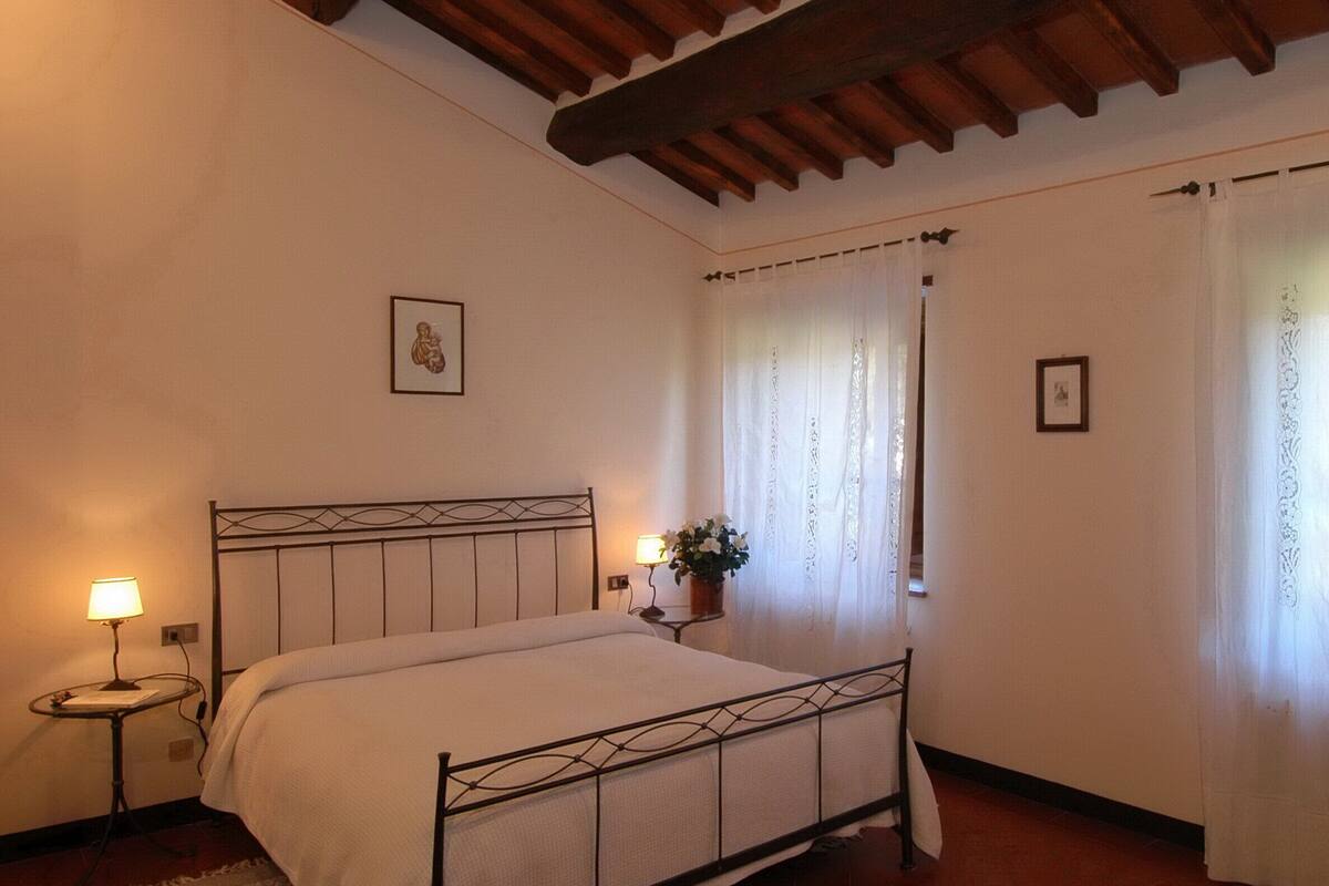 Een slaapkamer met een bed, nachtkastje, lamp, een potplant en een raam met gordijnen.