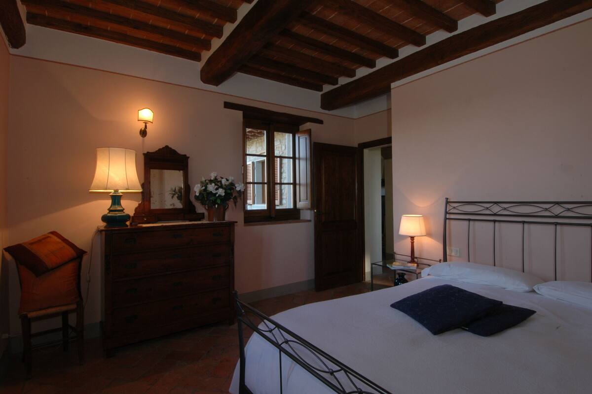 Een slaapkamer met een bed, een dressoir, een lamp en een raam.