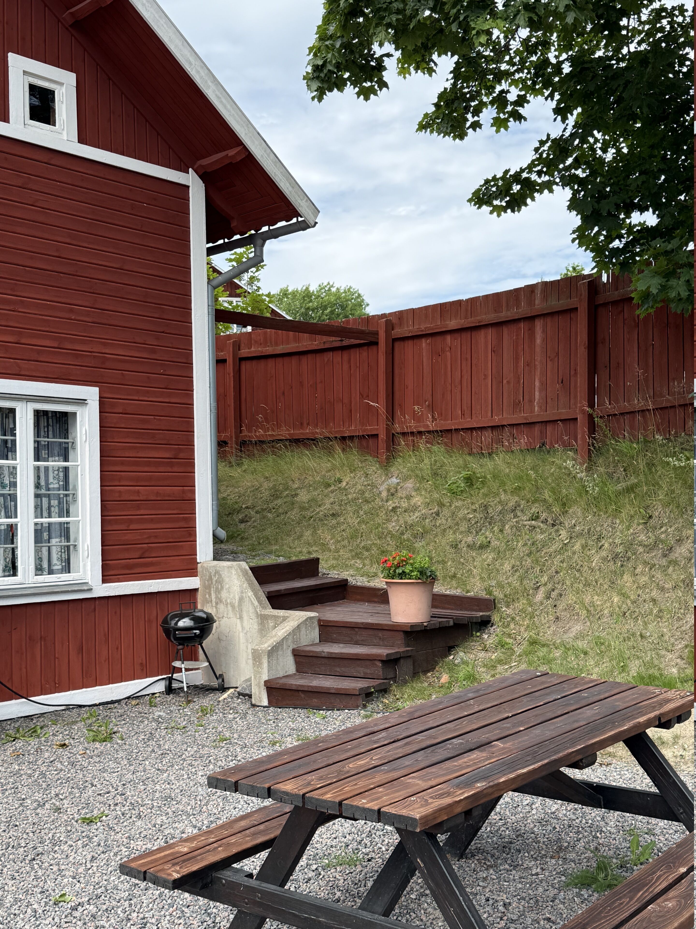 A red wooden house with a patio, a barbecue grill, and a wooden table.