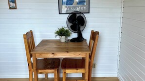A dining area with a wooden table and chairs, a black fan, and a framed picture on the wall. - Skeppsdockans Camping & Vandrarhem (Soderkoping)