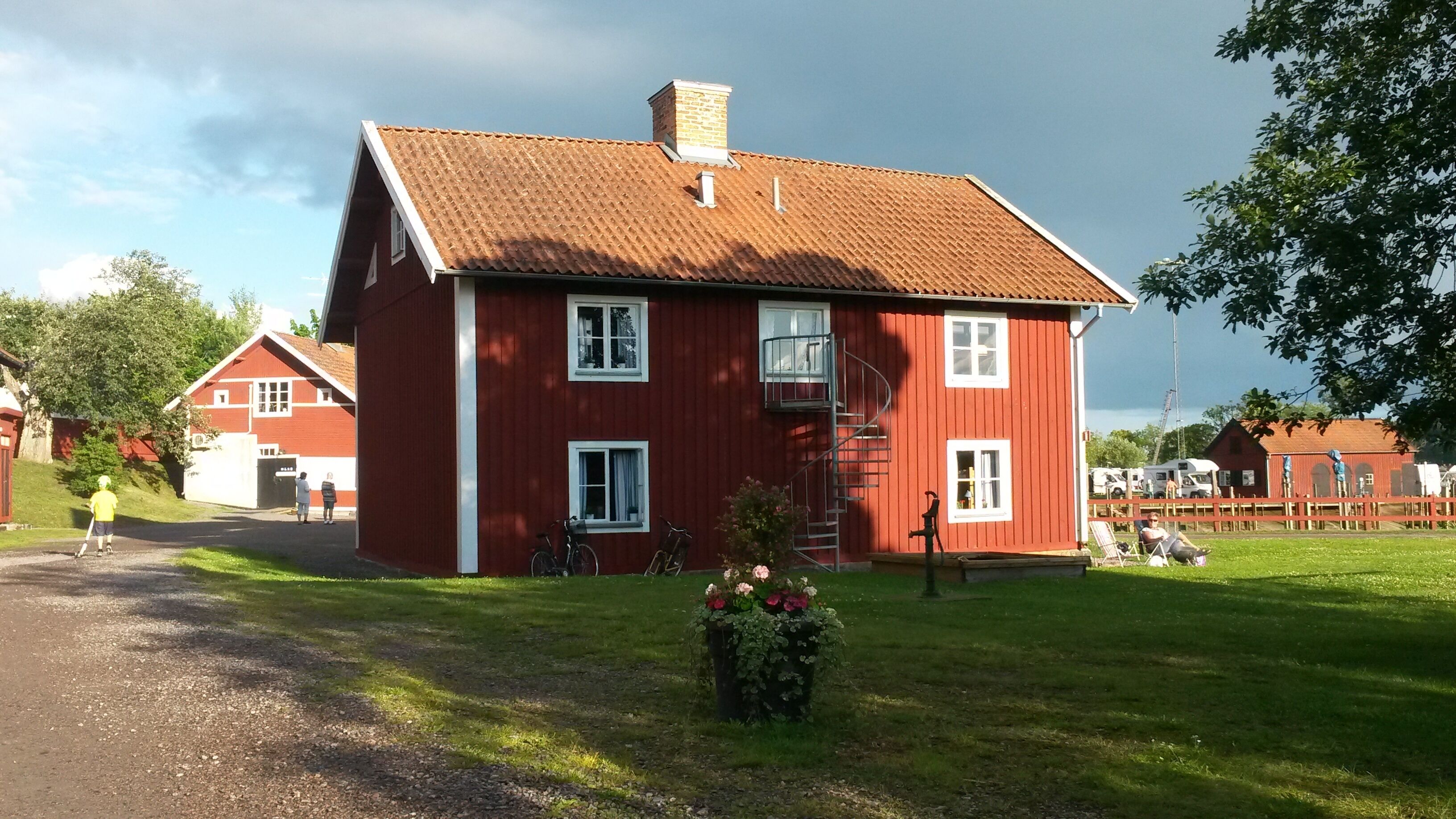 Ein rotes, zweistöckiges Haus mit einem Ziegeldach, einer kleinen Veranda und einem Garten mit Blumen.