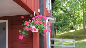 Un bâtiment en bois rouge avec une porte blanche et un panier à fleurs suspendu.