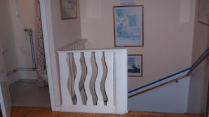 Un escalier en bois avec une rampe blanche, un rideau de douche à motifs et des tableaux encadrés accrochés au mur.