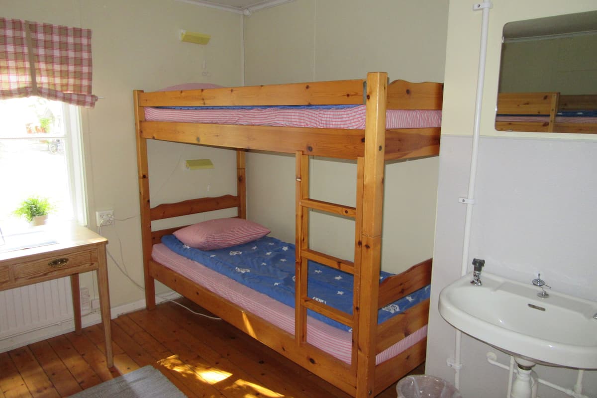 Una cama litera con escritorio y lavamanos en una habitación con suelo de madera.