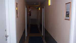 Un couloir d’hôtel avec un tapis bleu, des murs blancs et des portes donnant sur les chambres.