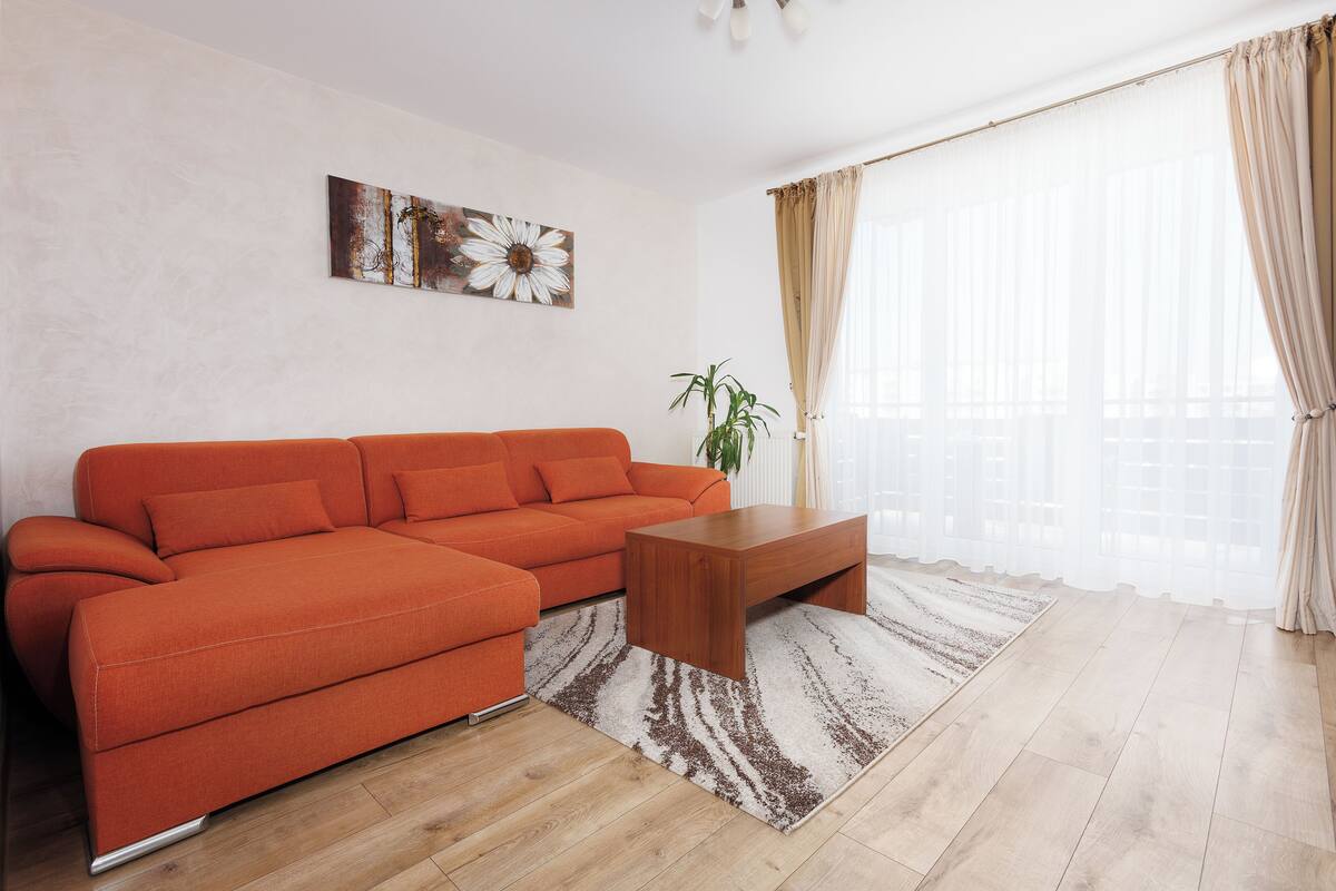 A modern living room with a sectional sofa, a wooden coffee table, and a large window with sheer curtains.