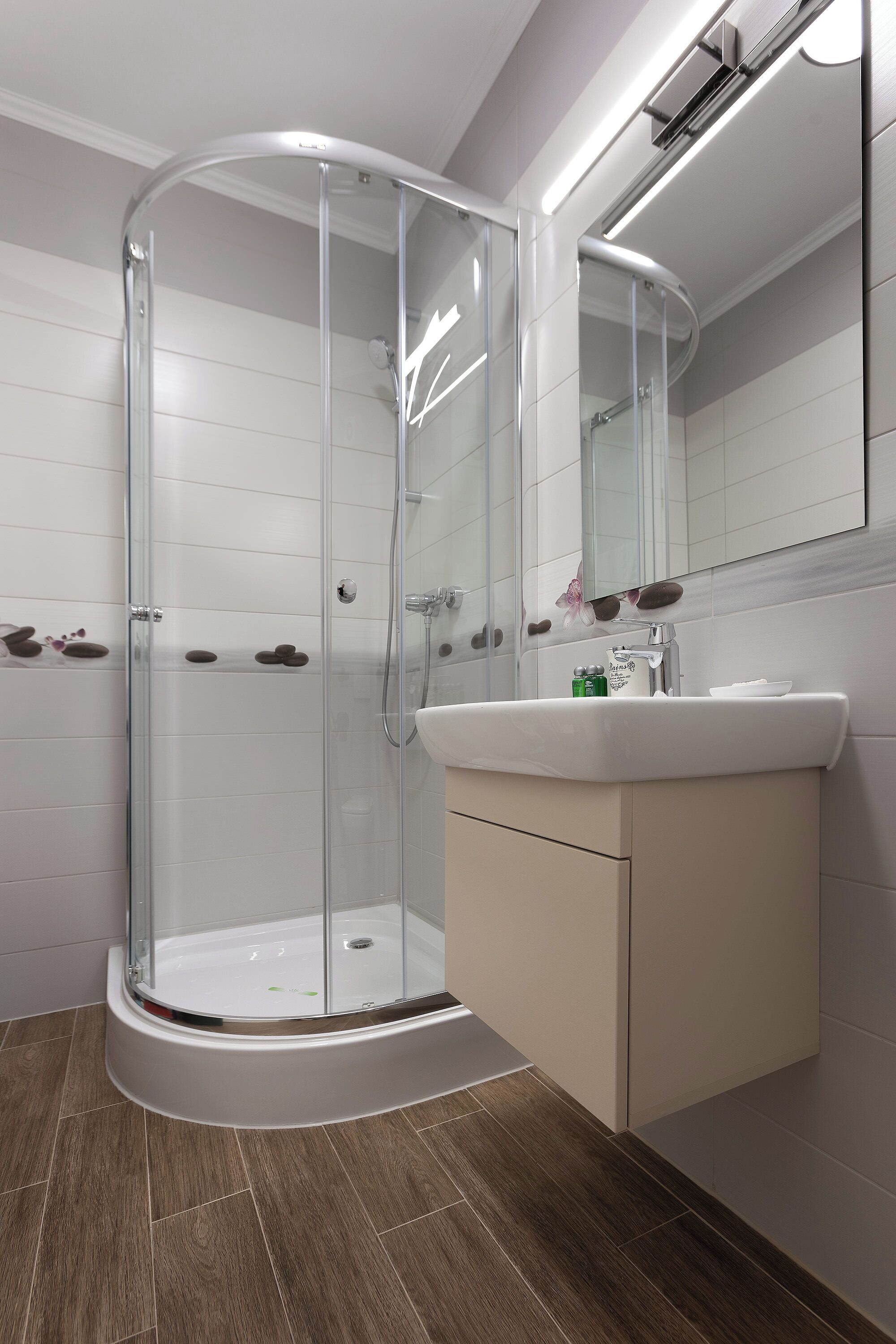 Un baño moderno con ducha envuelta en vidrio, un lavamanos blanco y un espejo encima.