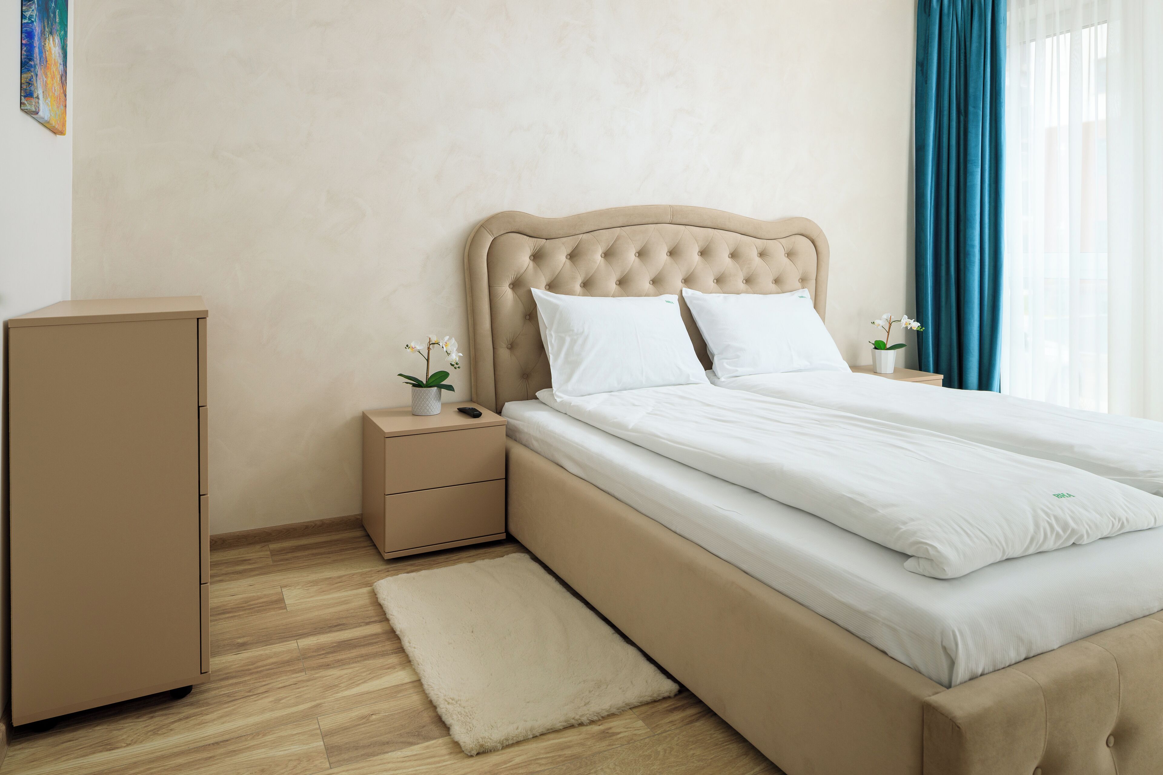 Une chambre à coucher avec un grand lit, une table de chevet, une commode et une fenêtre avec des rideaux.