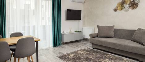 Una sala moderna con una mesa de comedor de madera, sillas grises, un sofá gris, una alfombra estampada y un televisor montado en la pared.